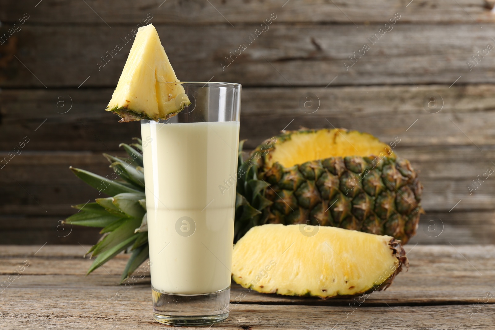 Photo of Tasty pineapple smoothie in glass and fruit on wooden table, closeup