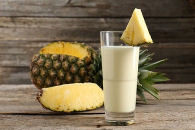 Photo of Tasty pineapple smoothie in glass and fruit on wooden table, closeup