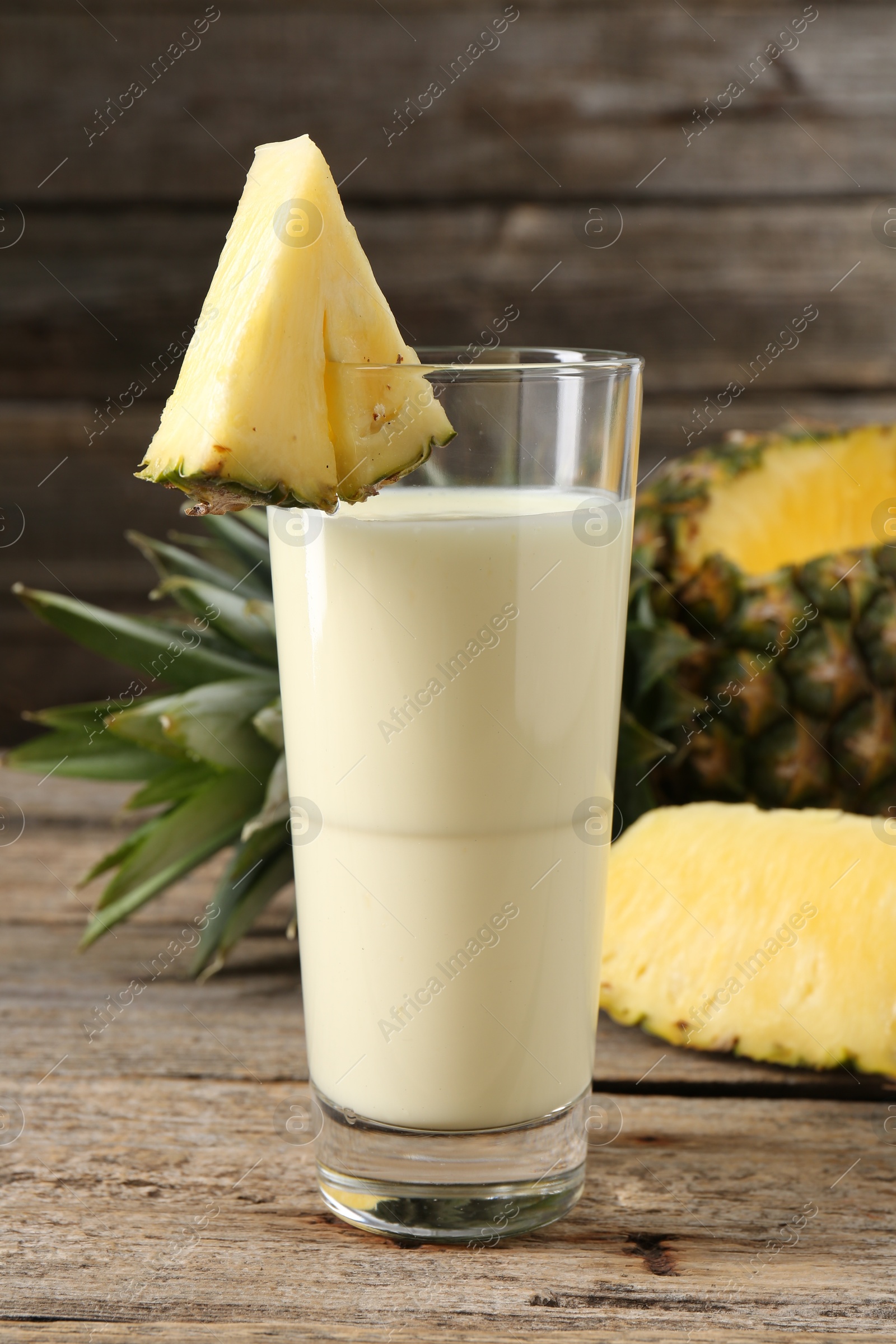 Photo of Tasty pineapple smoothie in glass and fruit on wooden table, closeup