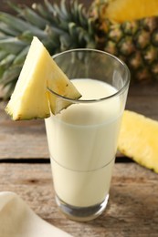 Photo of Tasty pineapple smoothie in glass and fruit on wooden table, closeup