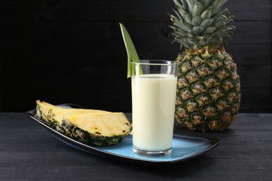 Photo of Tasty pineapple smoothie in glass and fruit on black wooden table