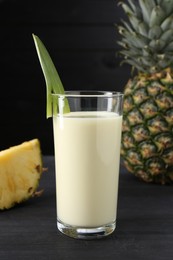 Photo of Tasty pineapple smoothie in glass and fruit on black wooden table, closeup