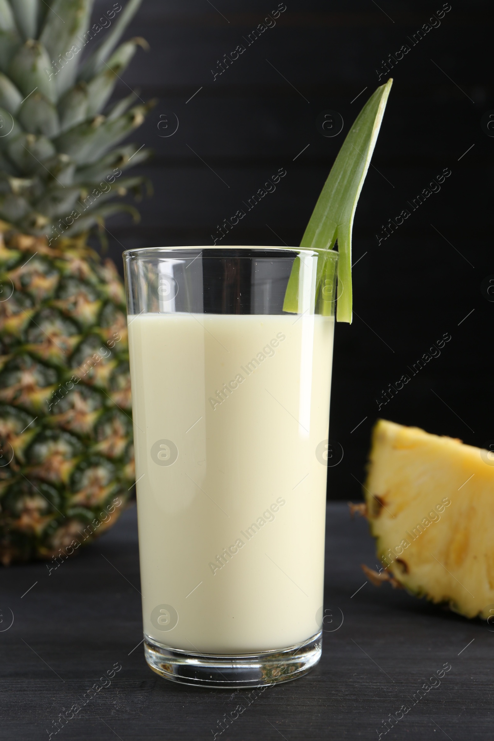 Photo of Tasty pineapple smoothie in glass and fruit on black wooden table, closeup