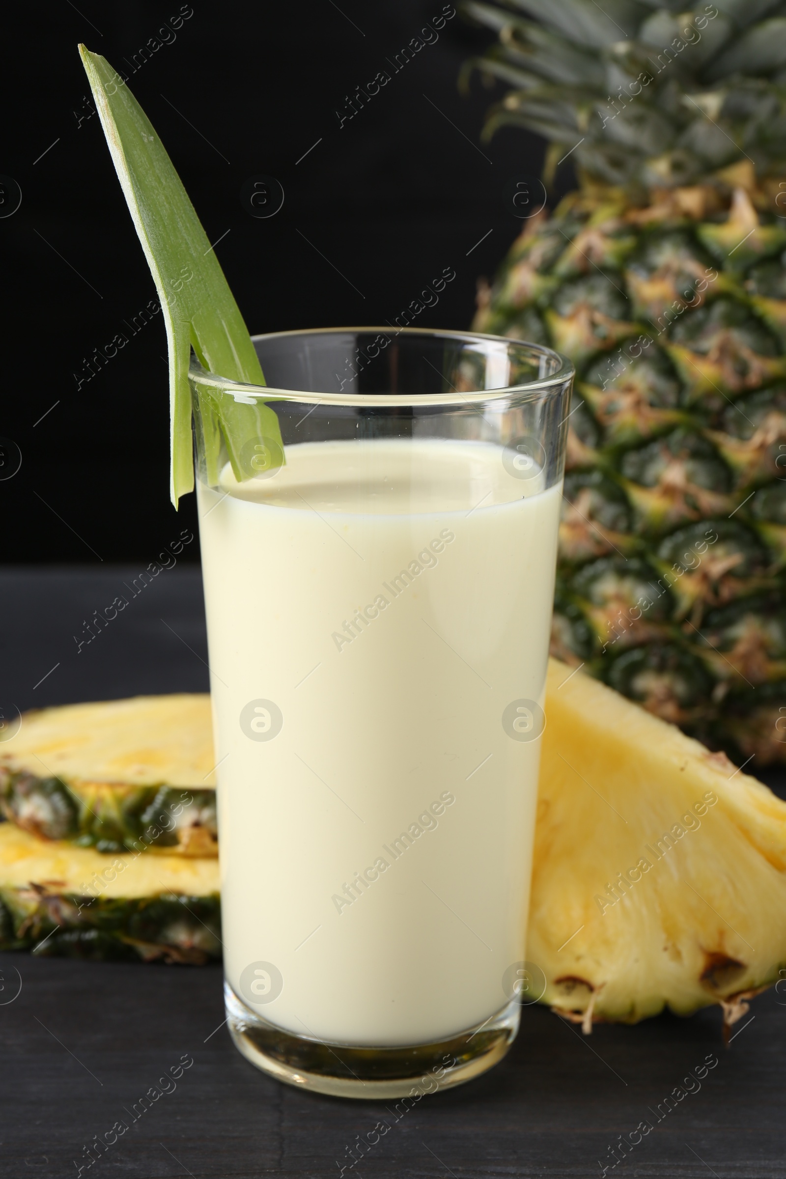 Photo of Tasty pineapple smoothie in glass and fruit on black wooden table, closeup