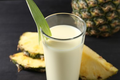 Photo of Tasty pineapple smoothie in glass and fruit on black table, closeup