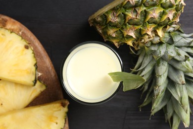 Photo of Tasty pineapple smoothie in glass and slices of fruit on black wooden table, flat lay