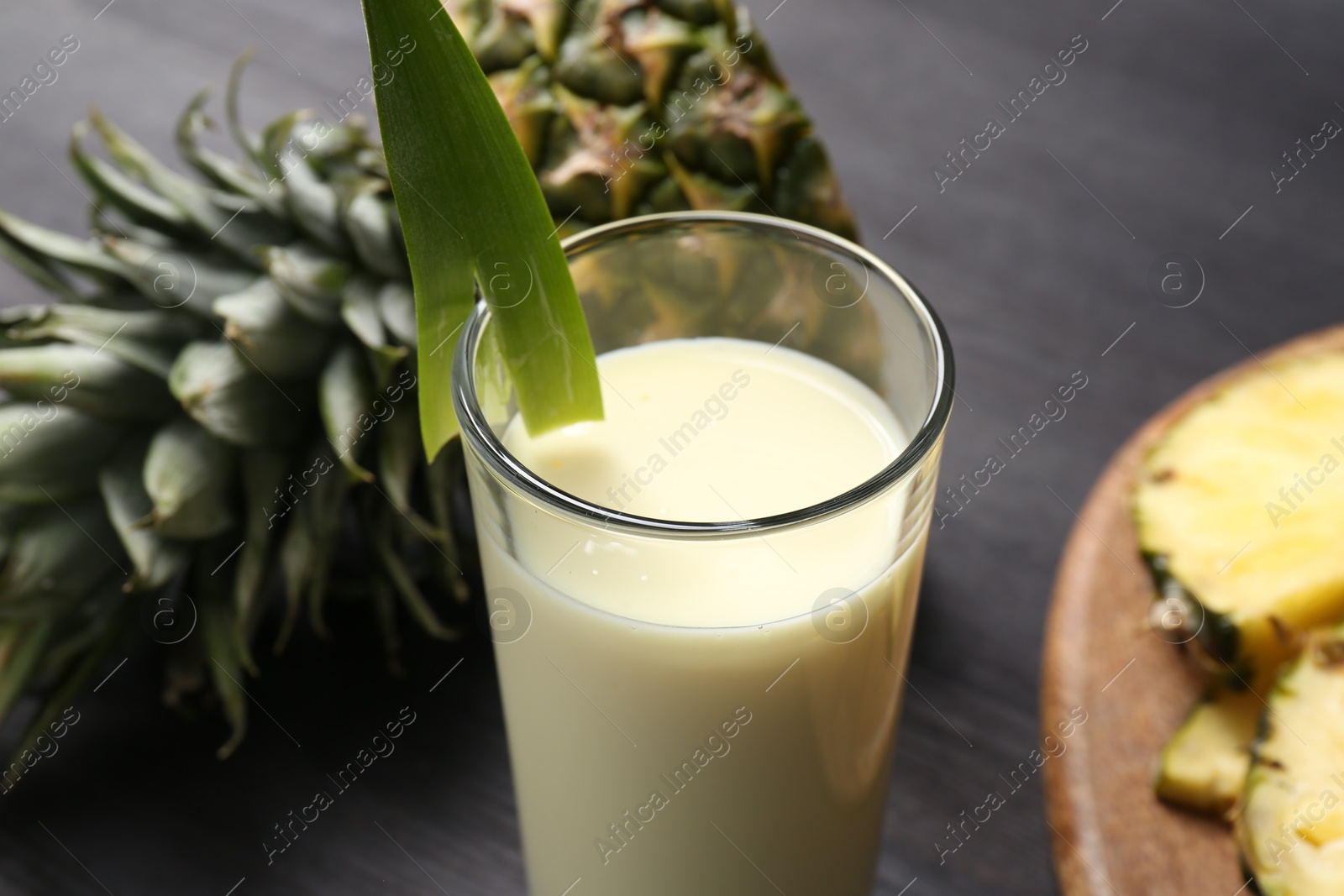 Photo of Tasty pineapple smoothie in glass and fruit on black table, closeup