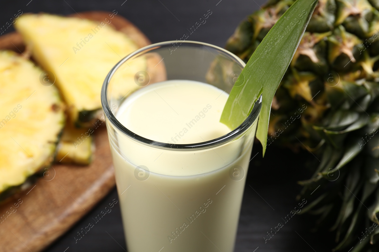 Photo of Tasty pineapple smoothie in glass and fruit on black table, closeup