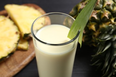 Photo of Tasty pineapple smoothie in glass and fruit on black table, closeup