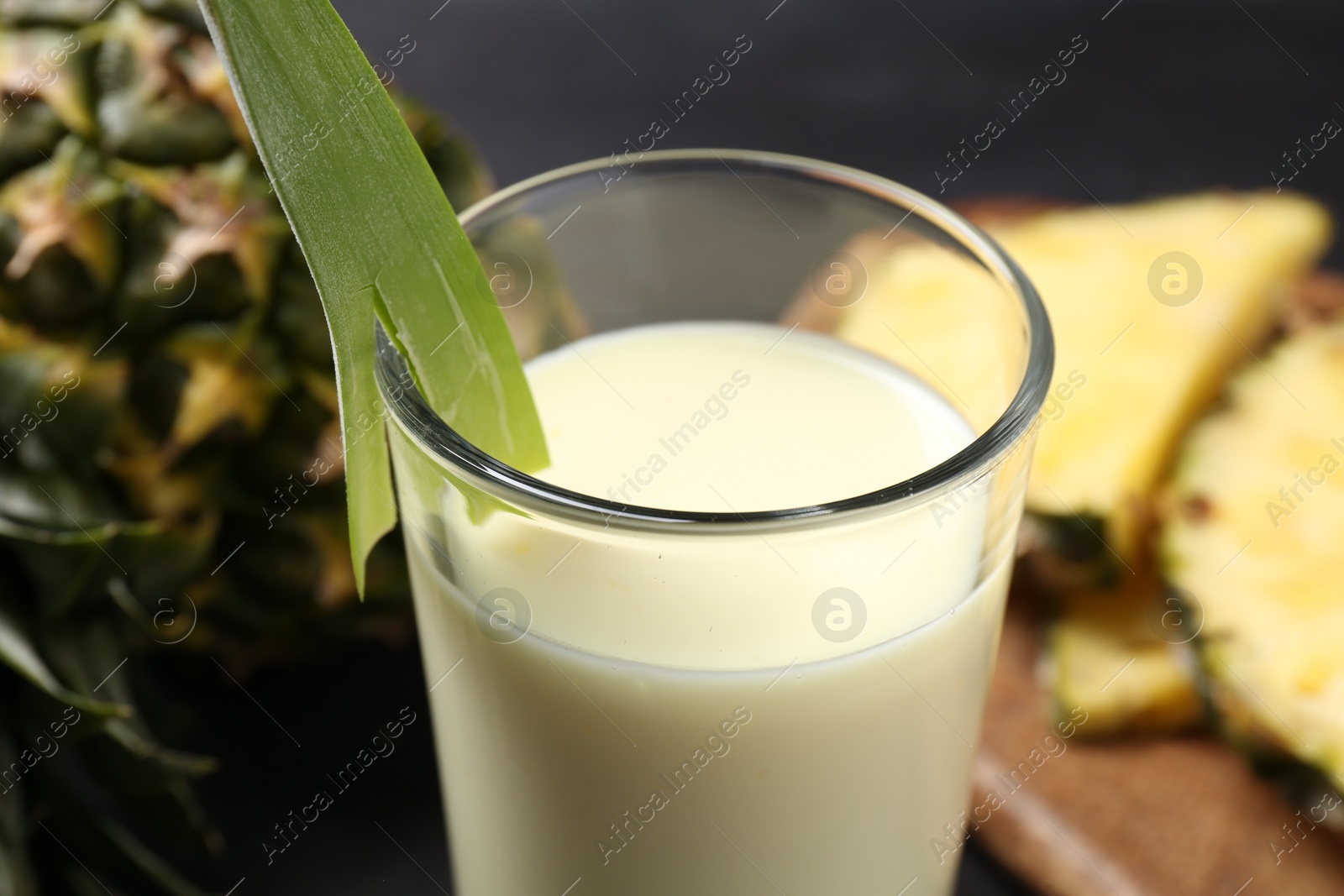 Photo of Tasty pineapple smoothie in glass and fruit on black table, closeup