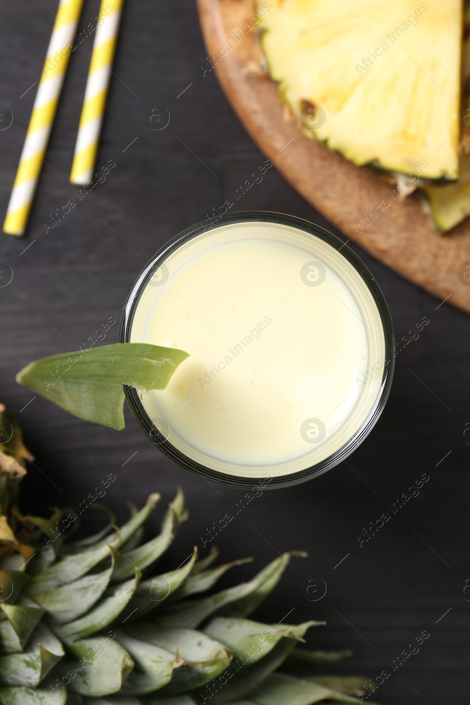 Photo of Tasty pineapple smoothie in glass and slices of fruit on black wooden table, flat lay