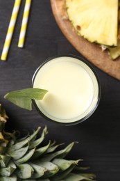 Photo of Tasty pineapple smoothie in glass and slices of fruit on black wooden table, flat lay