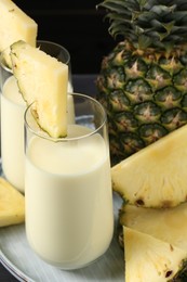 Photo of Tasty pineapple smoothie in glasses and fruit on black background, closeup