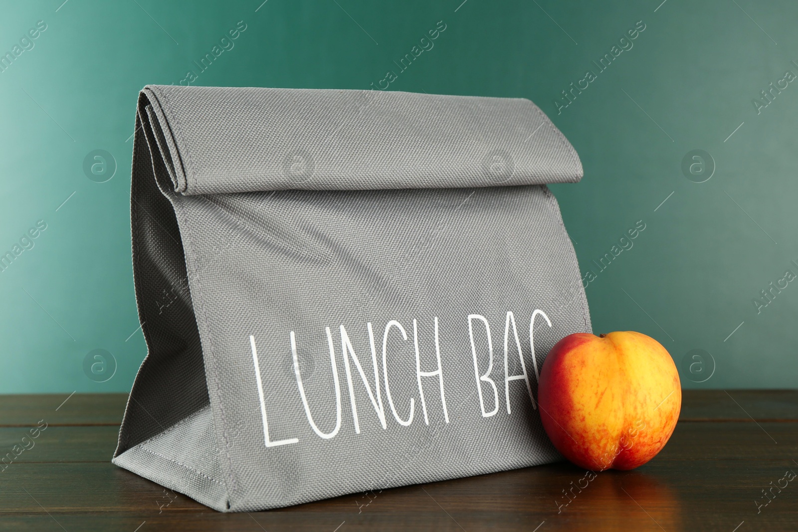 Photo of Lunch bag and fresh peach on wooden table against color background