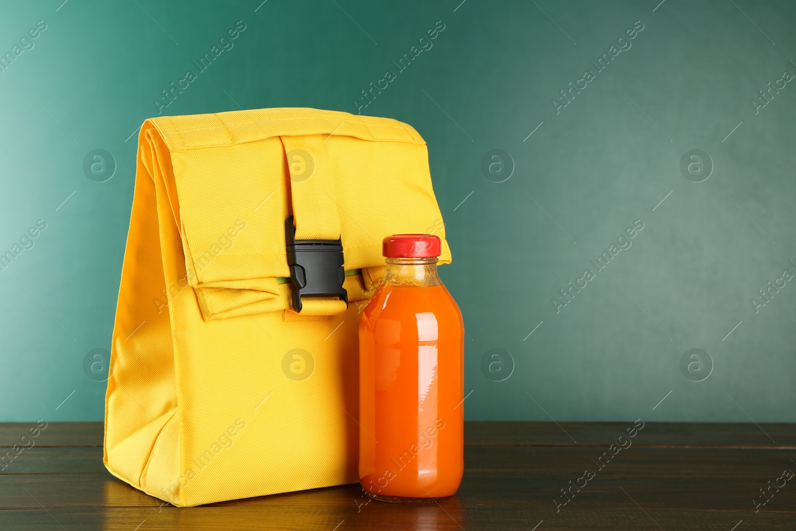 Photo of Lunch bag and bottle of juice on wooden table against color background, space for text