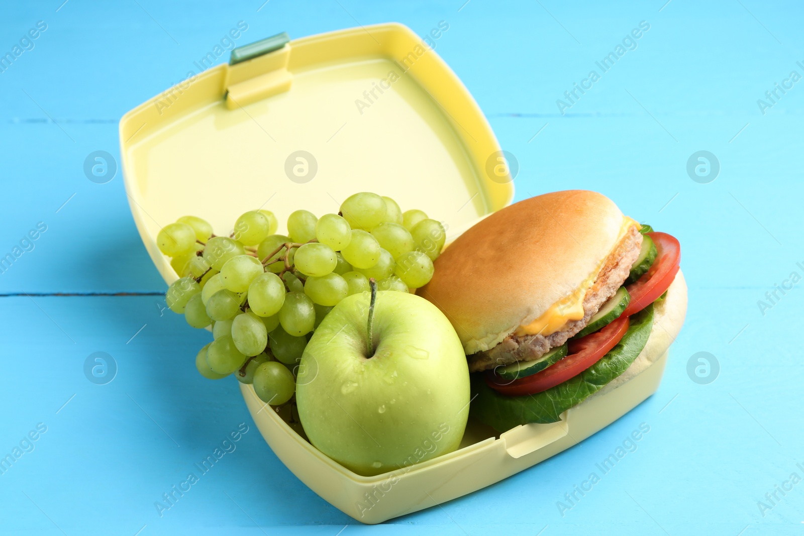 Photo of Plastic lunch box with burger and fresh fruits on light blue wooden table