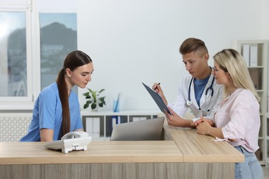 Photo of Professional receptionist and doctor working with patient at wooden desk in hospital