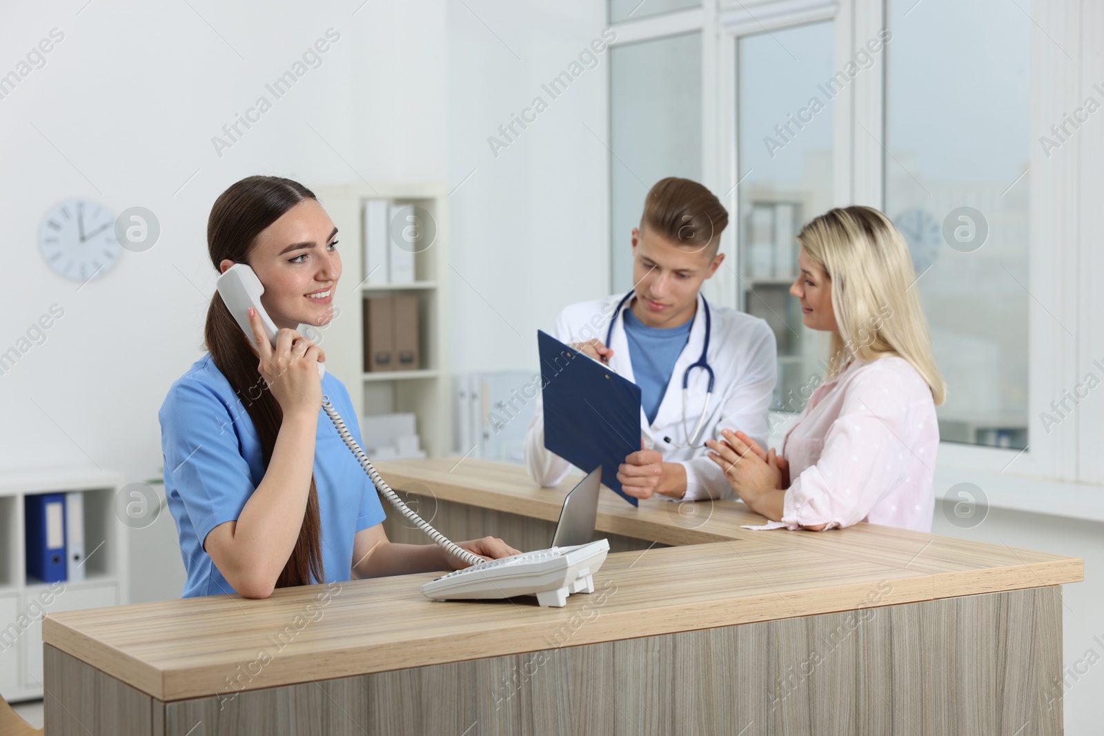 Photo of Professional receptionist and doctor working with patient at wooden desk in hospital