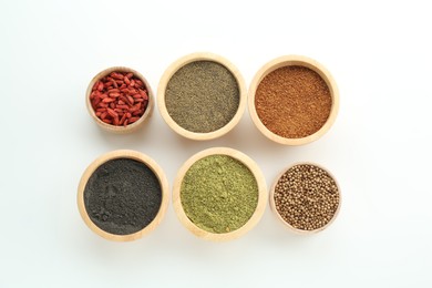 Photo of Different superfood powders and goji berries in bowls on white background, flat lay