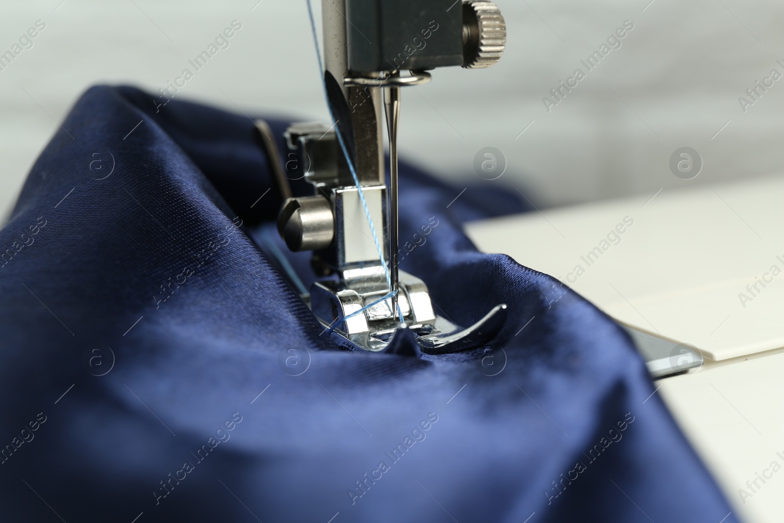 Photo of Sewing machine with blue fabric on light background, closeup