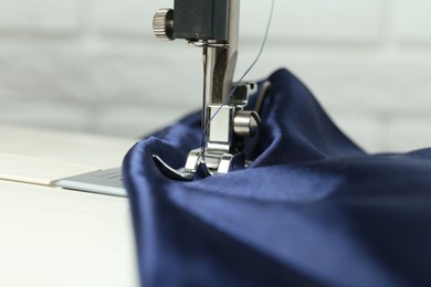 Photo of Sewing machine with blue fabric on light background, closeup