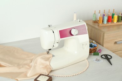 Sewing machine, beige fabric and craft accessories on wooden table indoors