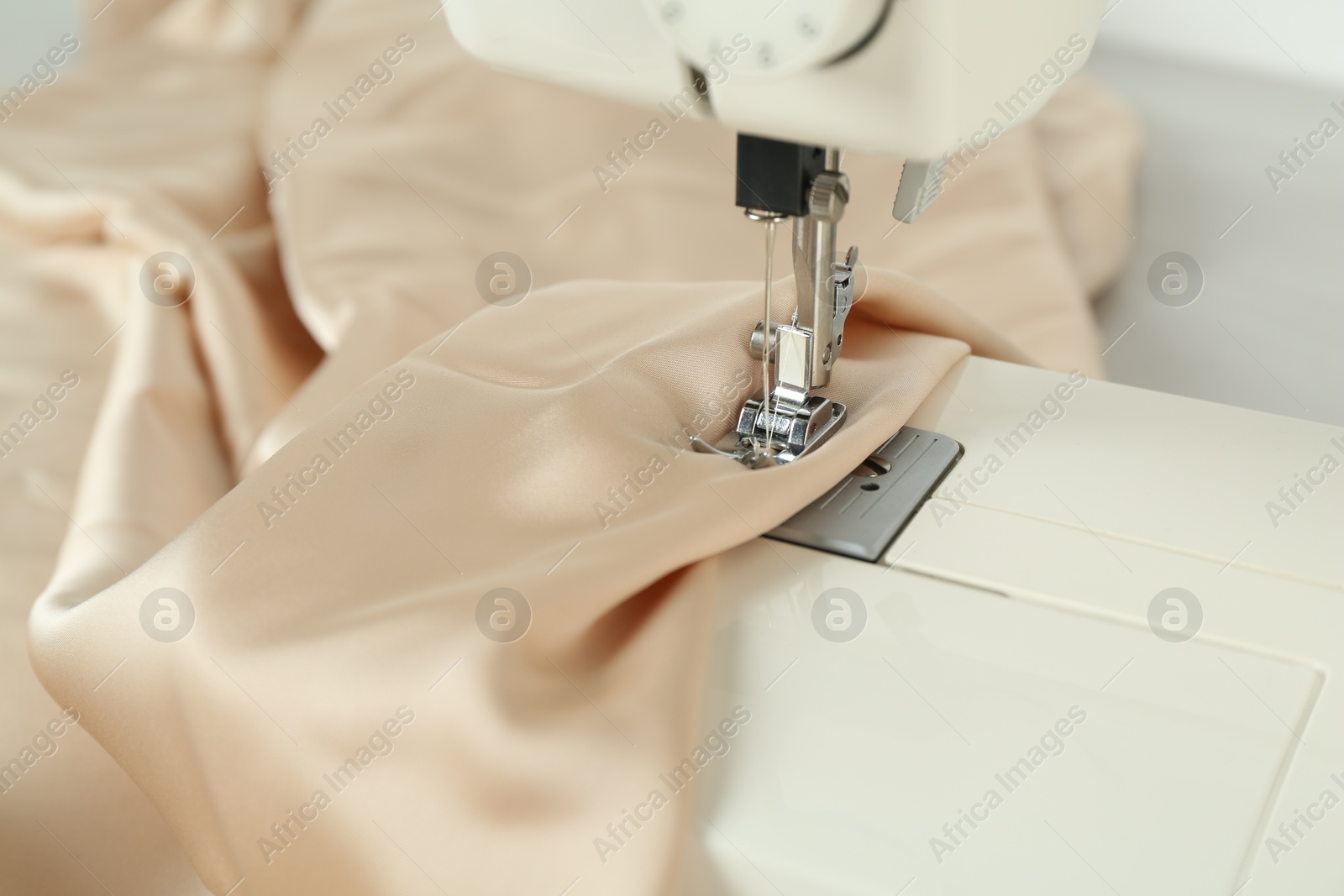 Photo of Sewing machine with beige fabric on table, closeup