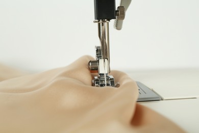 Photo of Sewing machine with beige fabric on white background, closeup