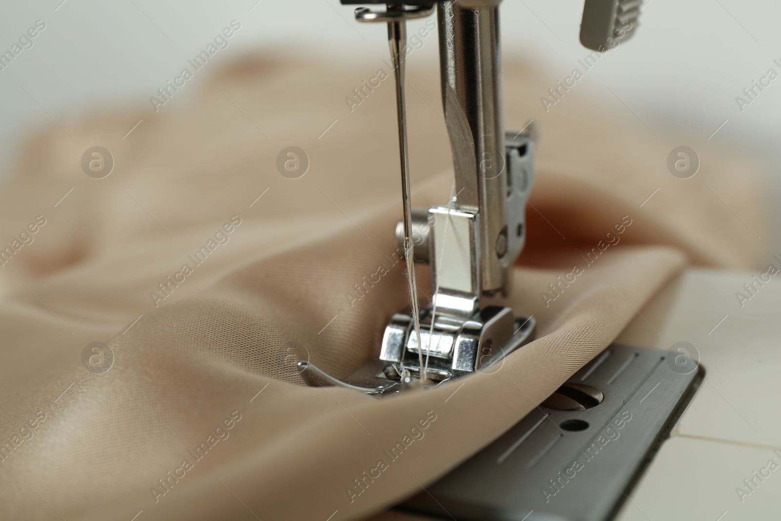 Photo of Sewing machine with beige fabric on light background, closeup