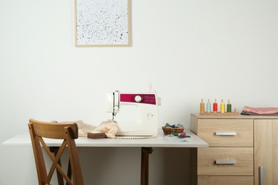 Sewing machine, beige fabric and craft accessories on light table indoors