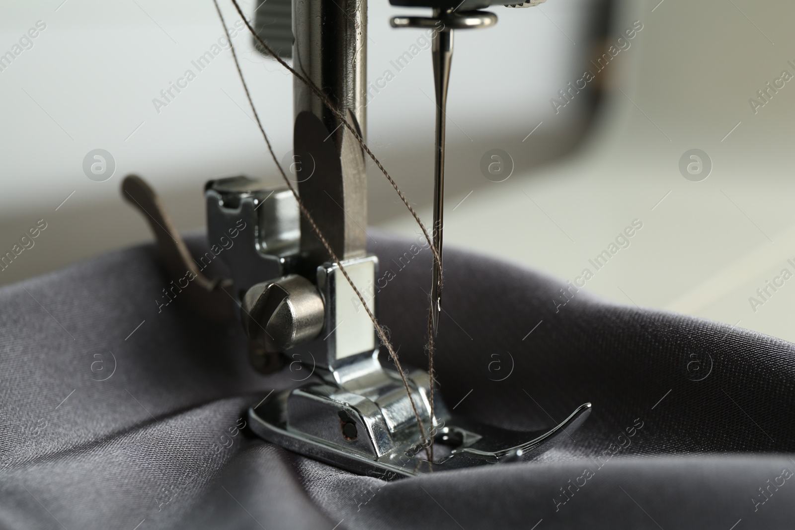 Photo of Sewing machine with gray fabric on light background, closeup