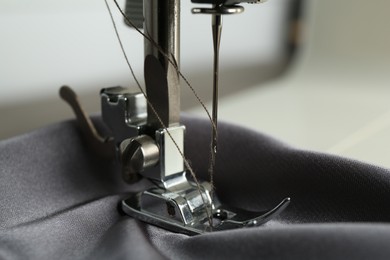 Sewing machine with gray fabric on light background, closeup