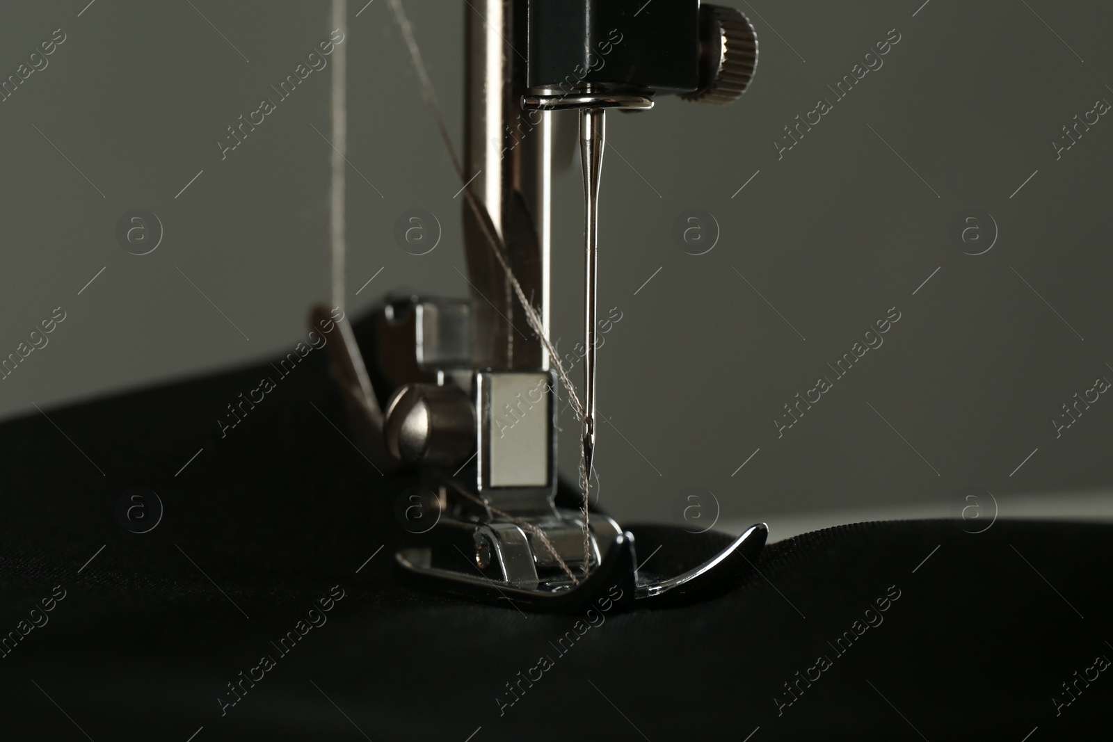 Photo of Sewing machine with black fabric on gray background, closeup