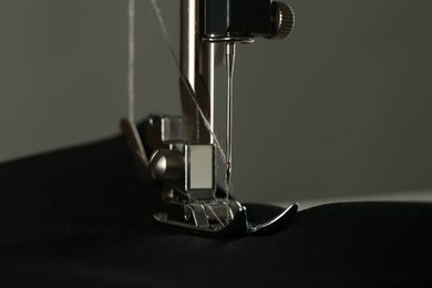 Sewing machine with black fabric on gray background, closeup