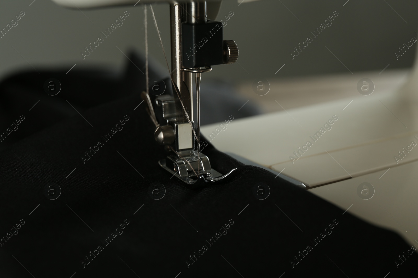 Photo of Sewing machine with black fabric on gray background, closeup