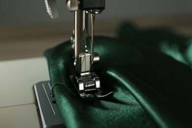 Sewing machine with green fabric on light background, closeup