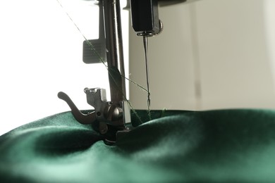 Sewing machine with green fabric on white background, closeup