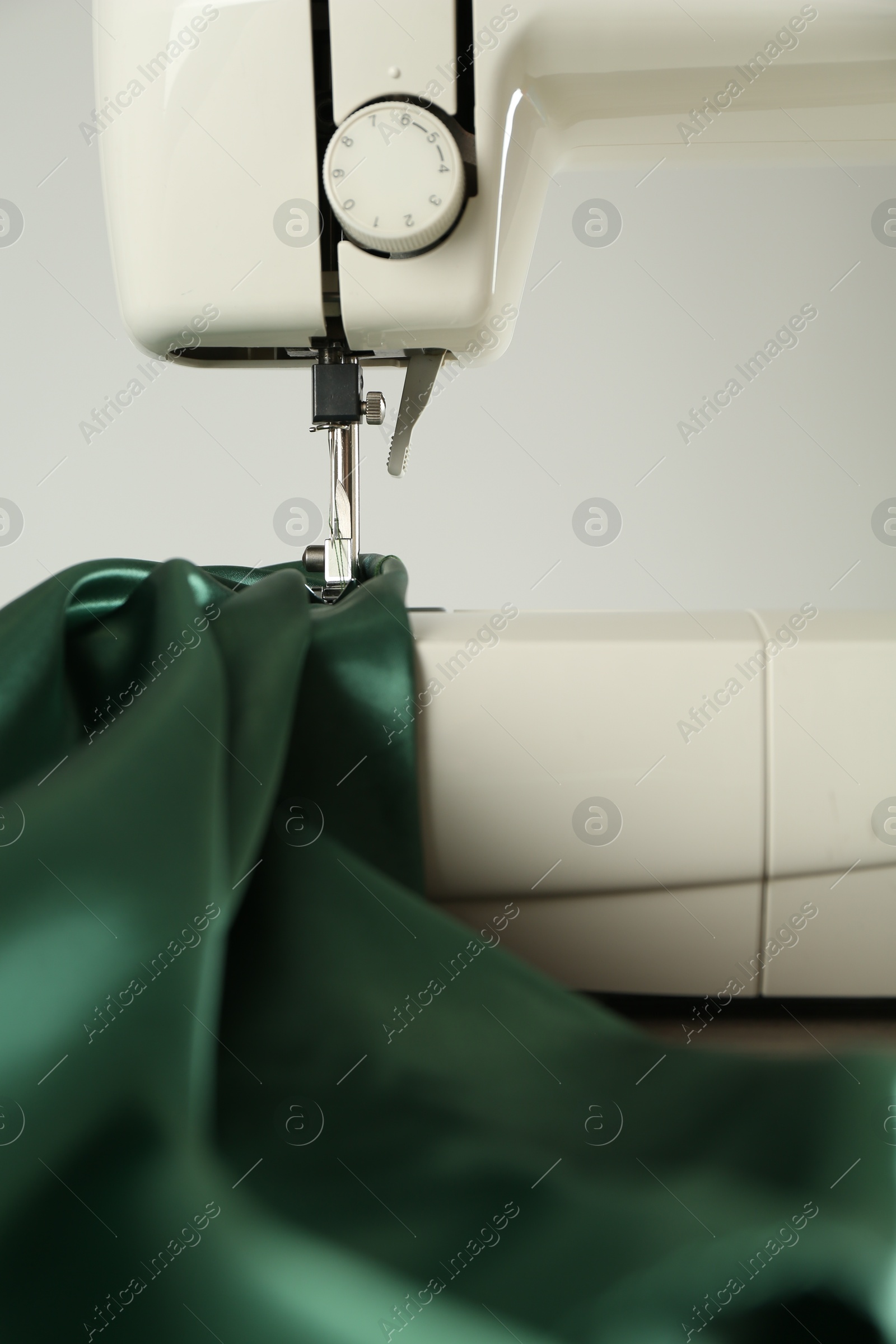 Photo of Sewing machine with green fabric on white background, closeup