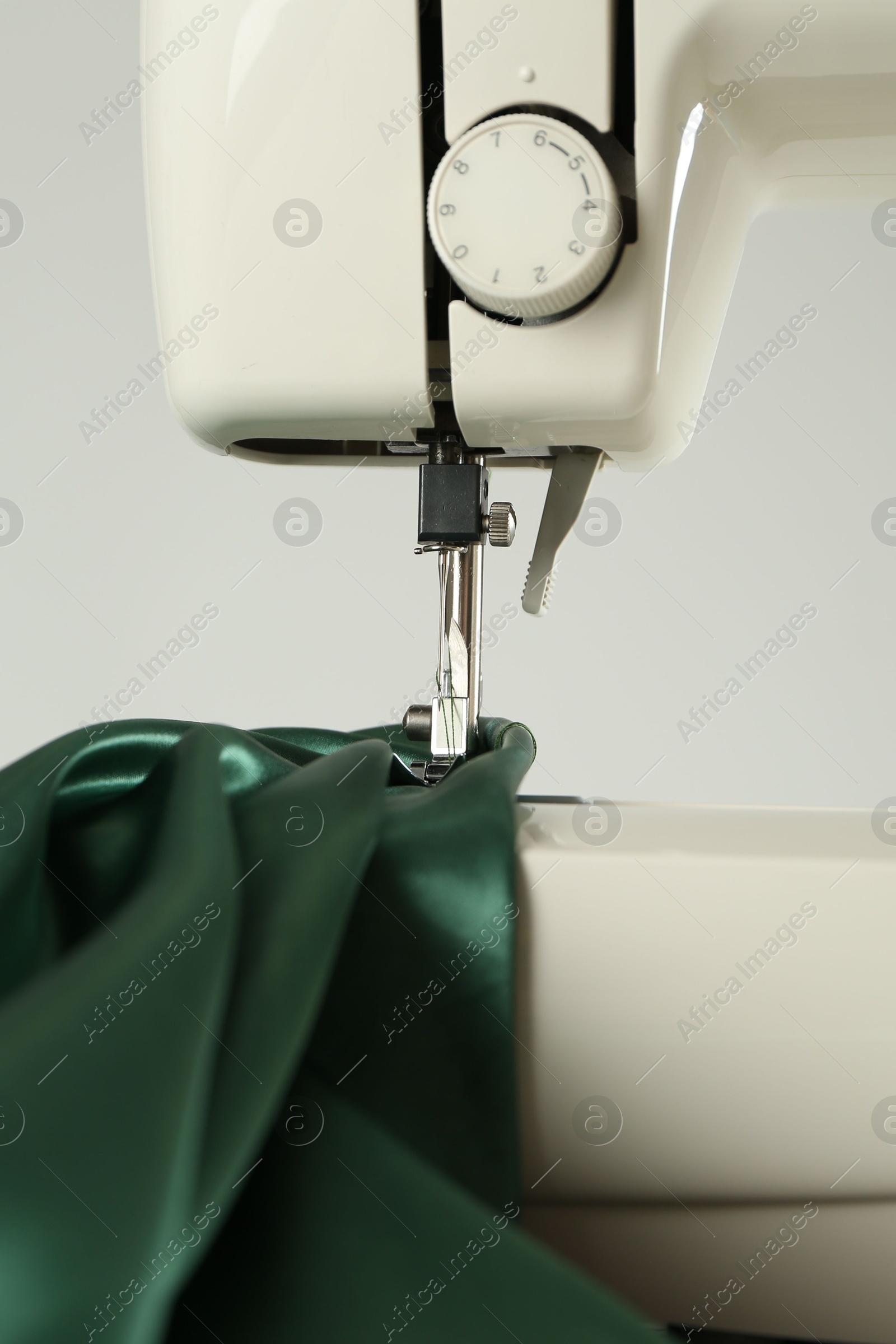 Photo of Sewing machine with green fabric on white background, closeup