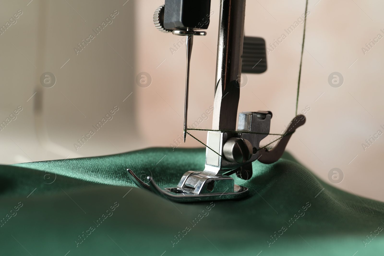 Photo of Sewing machine with green fabric on light background, closeup