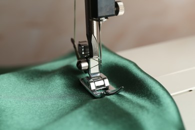 Photo of Sewing machine with green fabric on light background, closeup