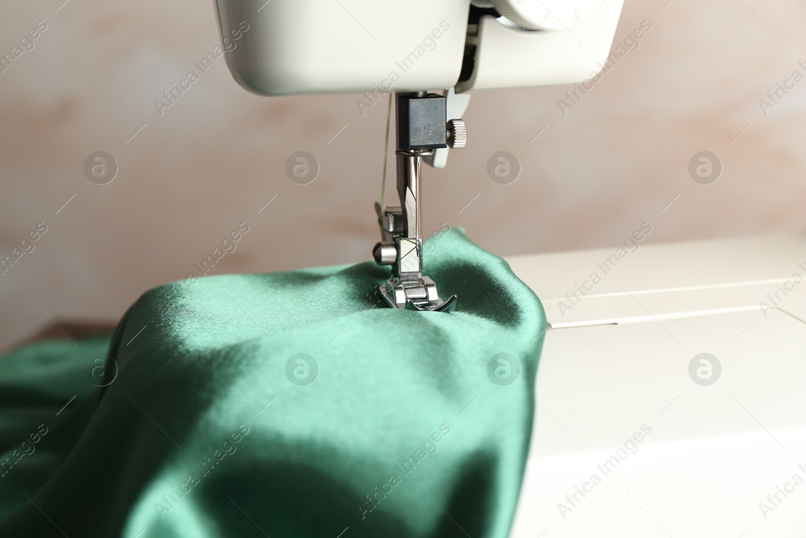 Photo of Sewing machine with green fabric on light background, closeup