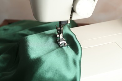 Sewing machine with green fabric on light background, closeup