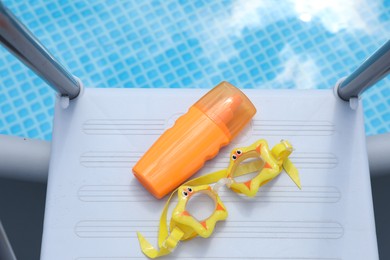 Bottle of sunscreen and swim goggles near swimming pool outdoors, top view