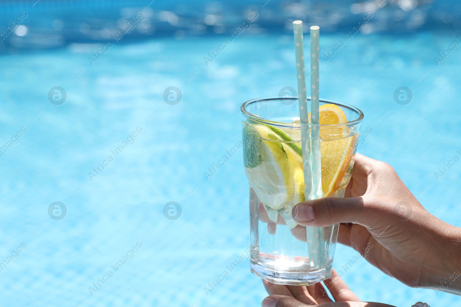 Photo of Woman holding tasty cocktail in glass near swimming pool outdoors, closeup