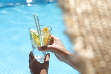 Photo of Woman holding tasty cocktail in glass near swimming pool outdoors, closeup