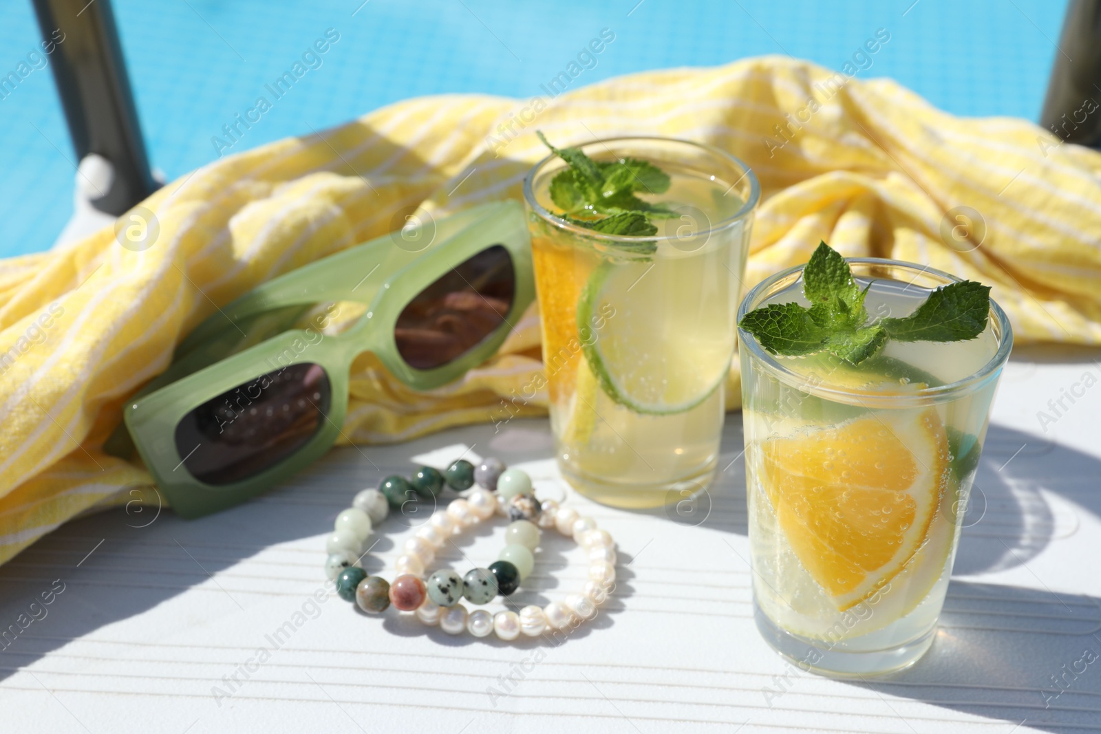 Photo of Tasty cocktail in glasses and sunglasses near swimming pool outdoors