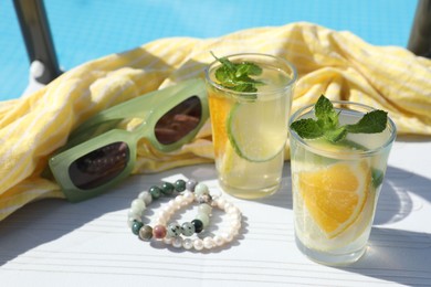 Photo of Tasty cocktail in glasses and sunglasses near swimming pool outdoors