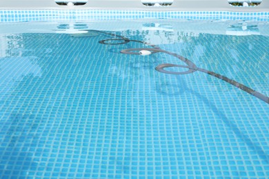 Photo of One robotic cleaner with pipe in swimming pool outdoors