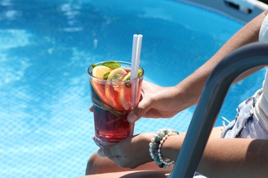 Photo of Woman holding tasty cocktail in glass near swimming pool outdoors, closeup